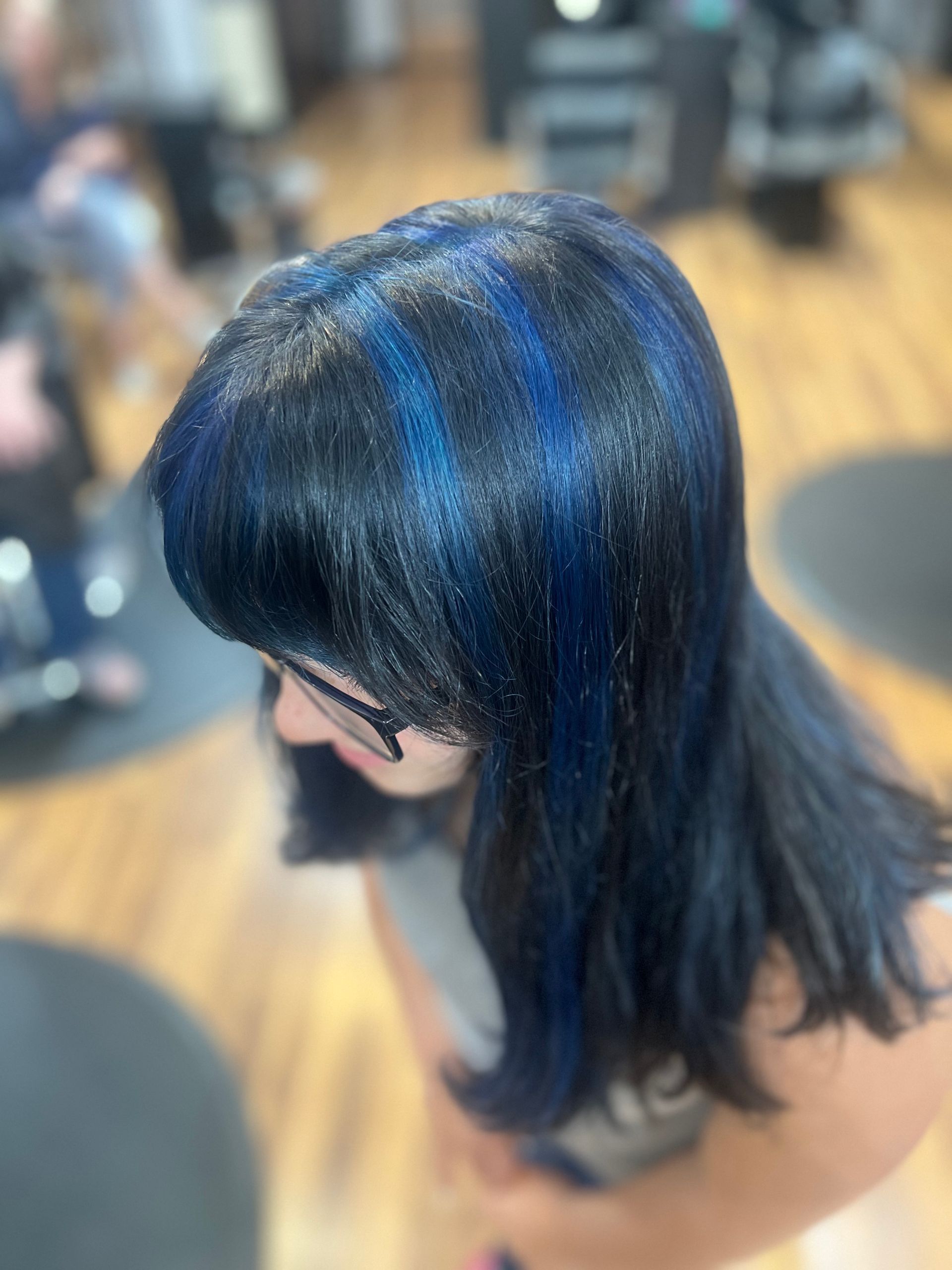 A woman with black hair and blue highlights is standing in a salon.