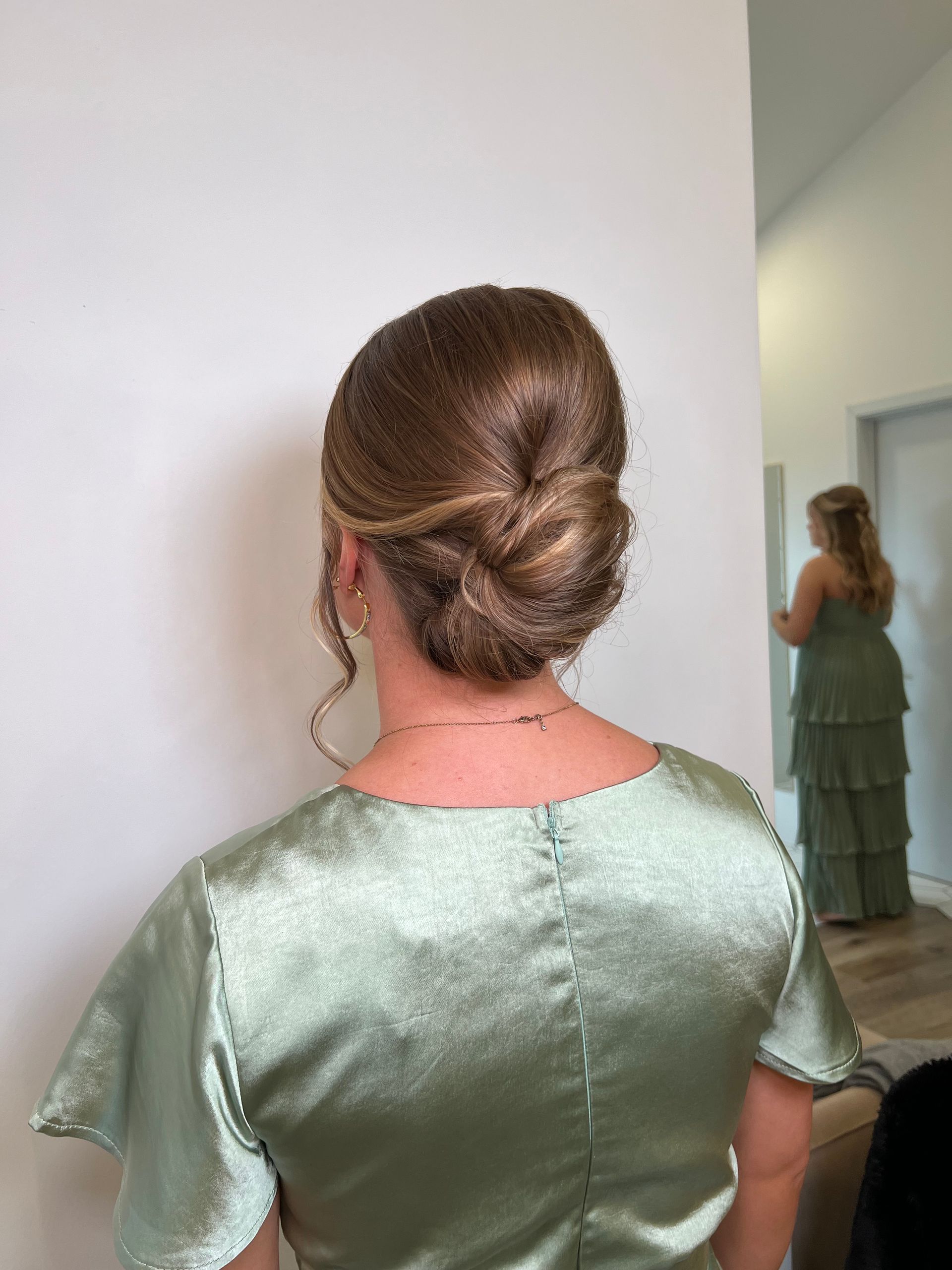A woman in a green dress is standing in front of a mirror.