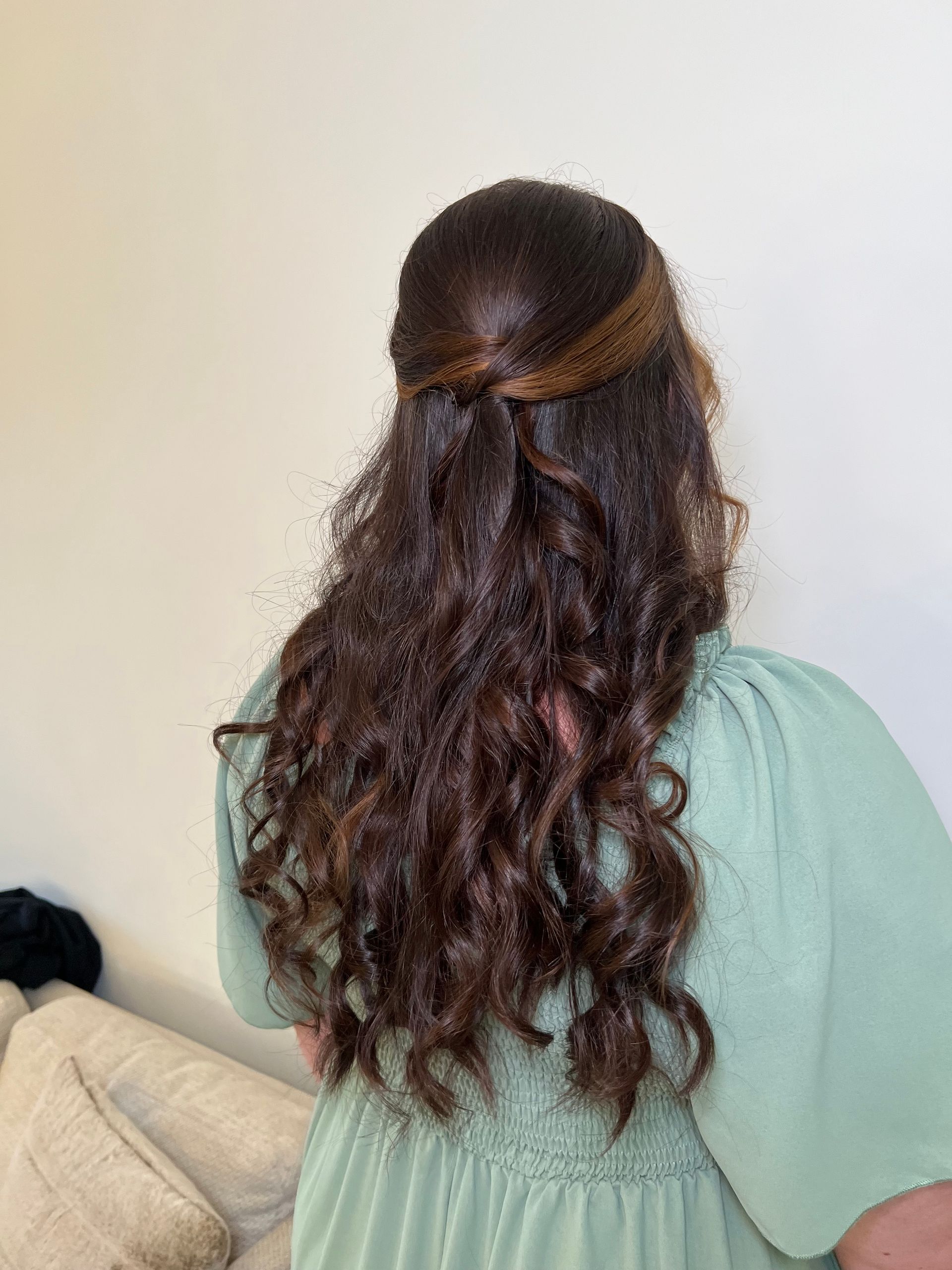 A woman in a green dress is wearing her hair in a half up half down hairstyle.