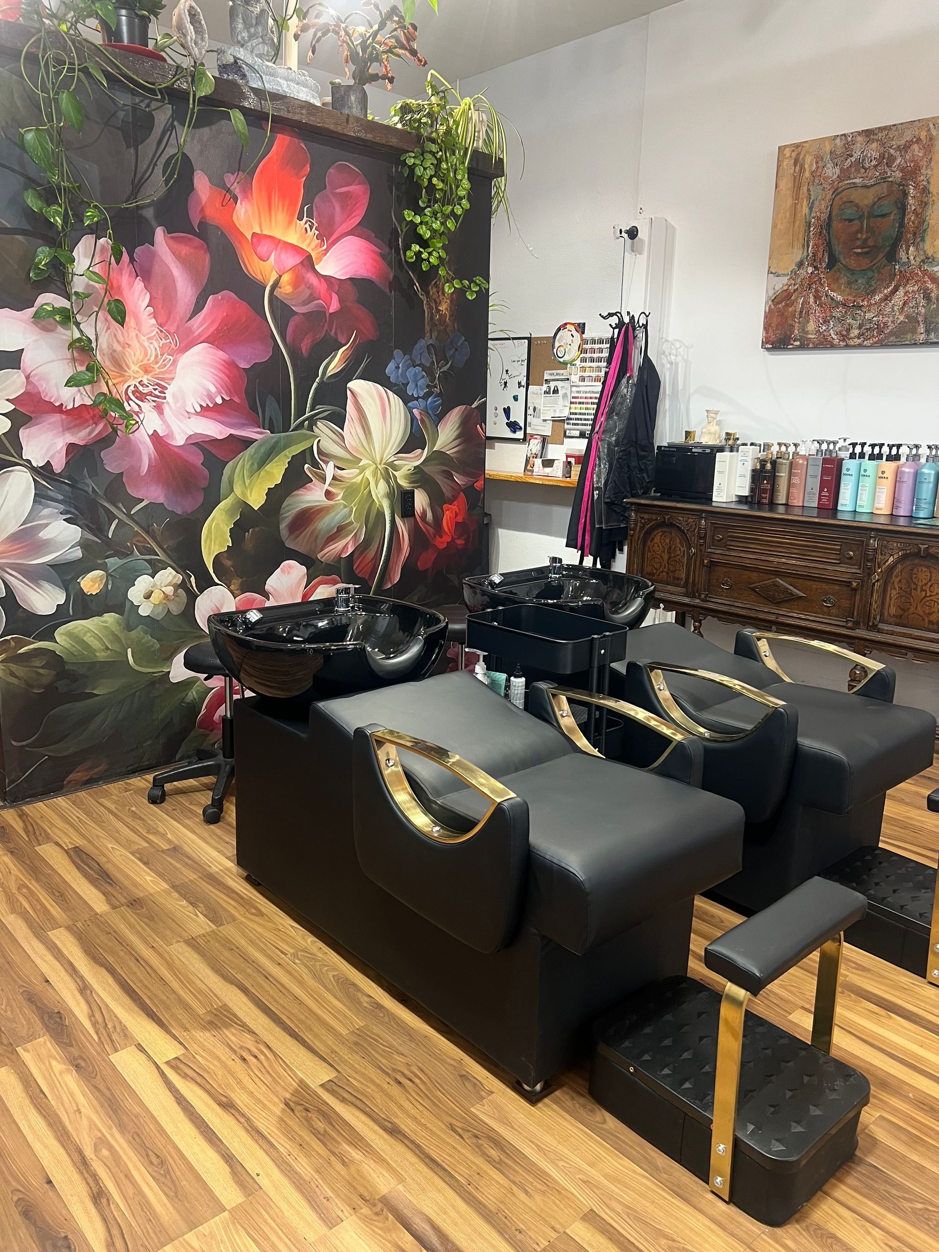 Salon with black wash stations, gold accents, floral backdrop, wooden floor, and product display.