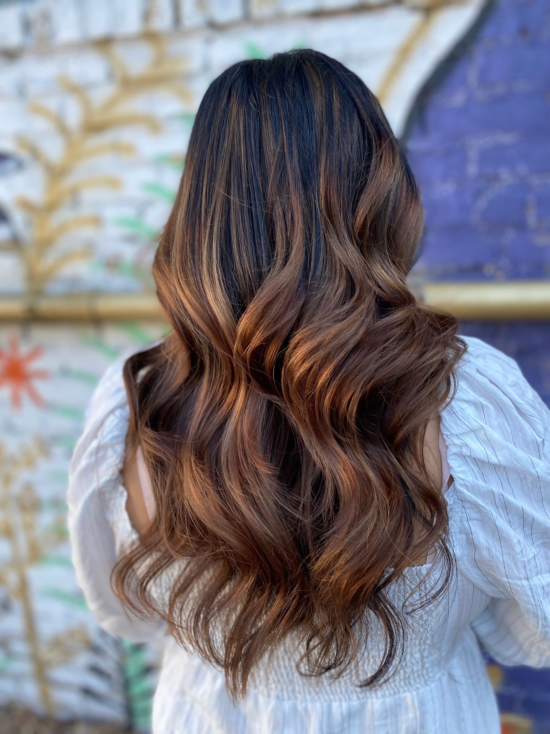 A woman with long brown hair is standing in front of a graffiti wall.