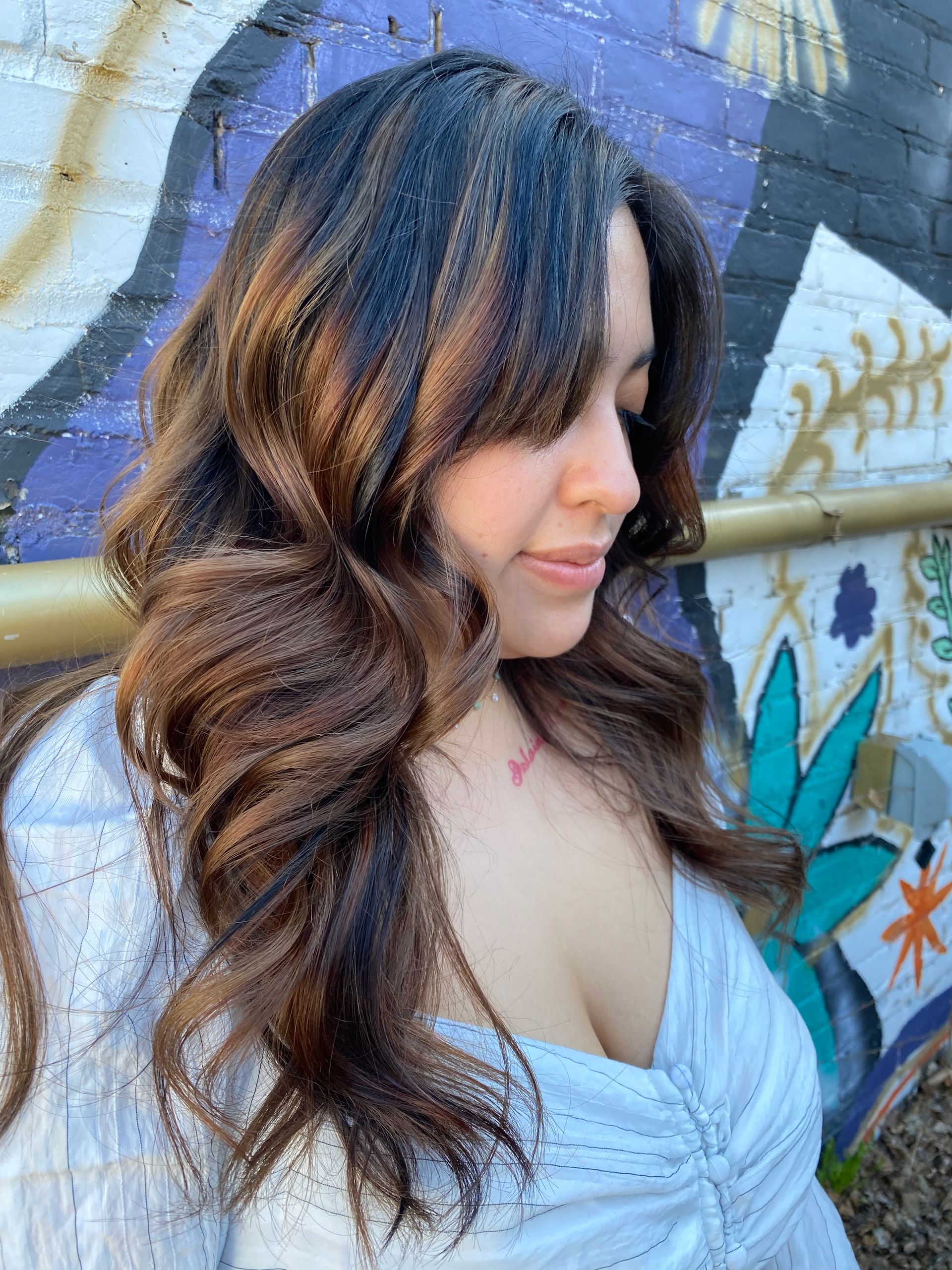 A woman with long brown hair is standing in front of a graffiti wall.