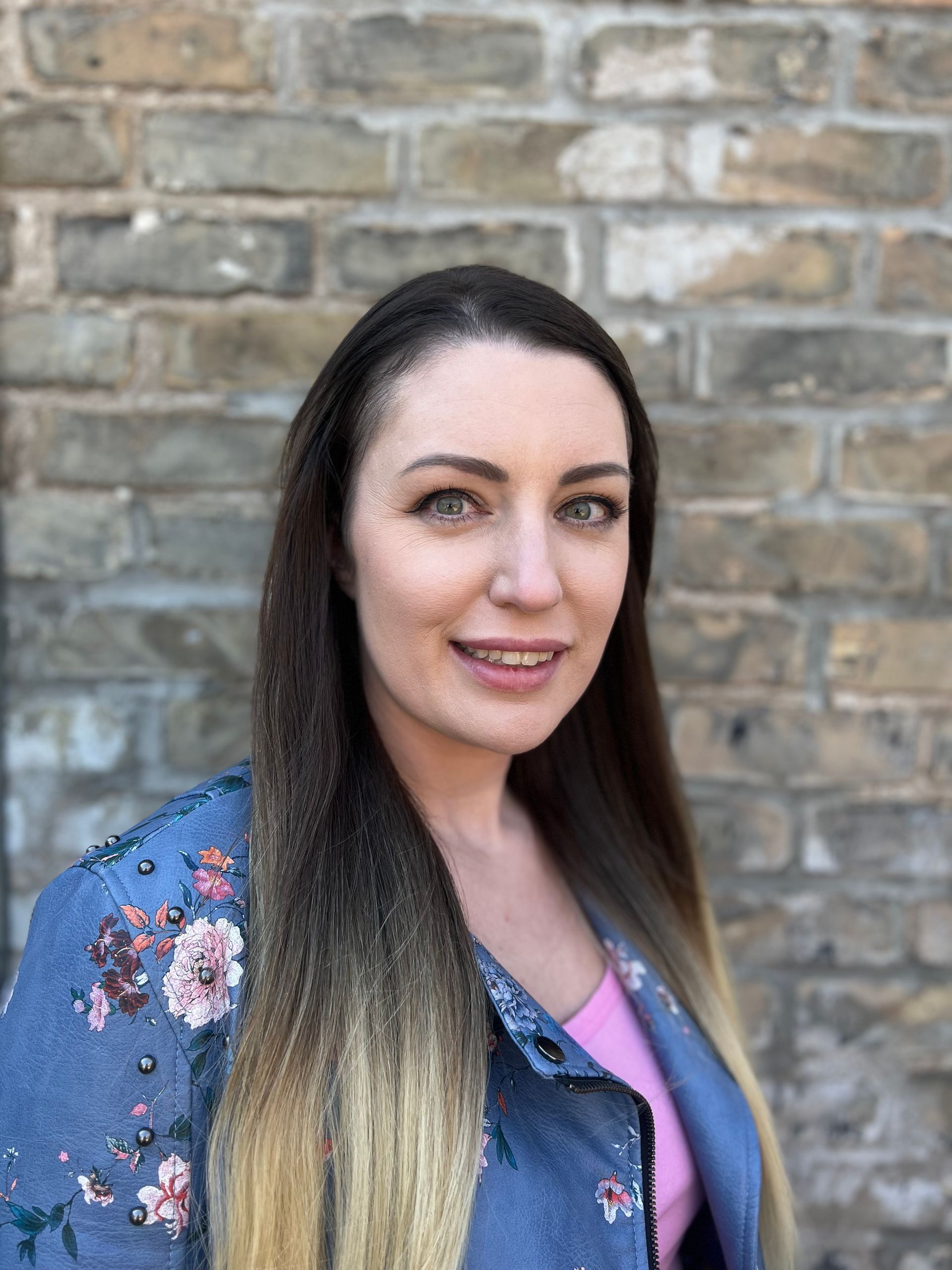 A woman with long hair is standing in front of a brick wall.