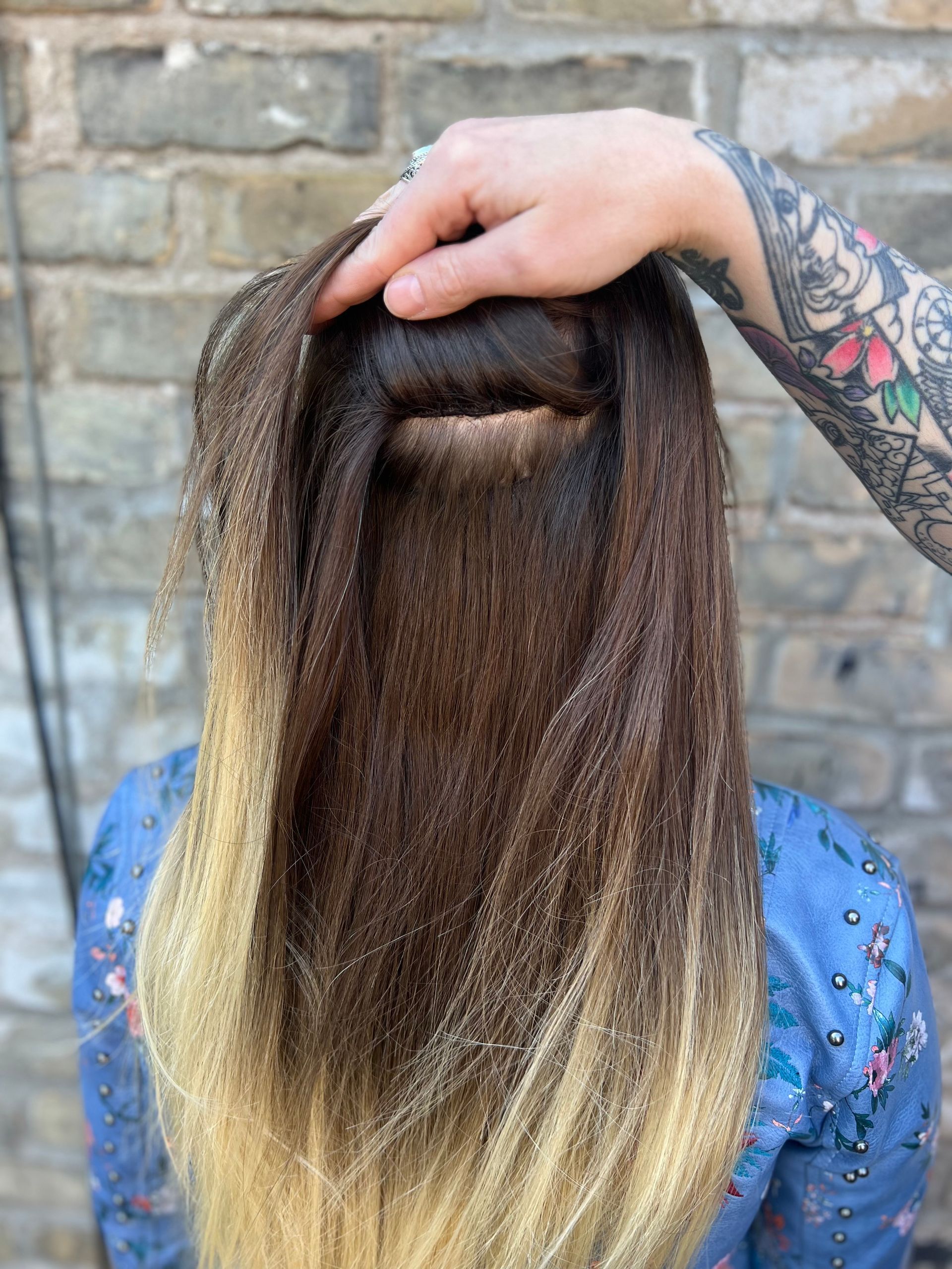 A person is touching a woman 's hair in front of a brick wall.