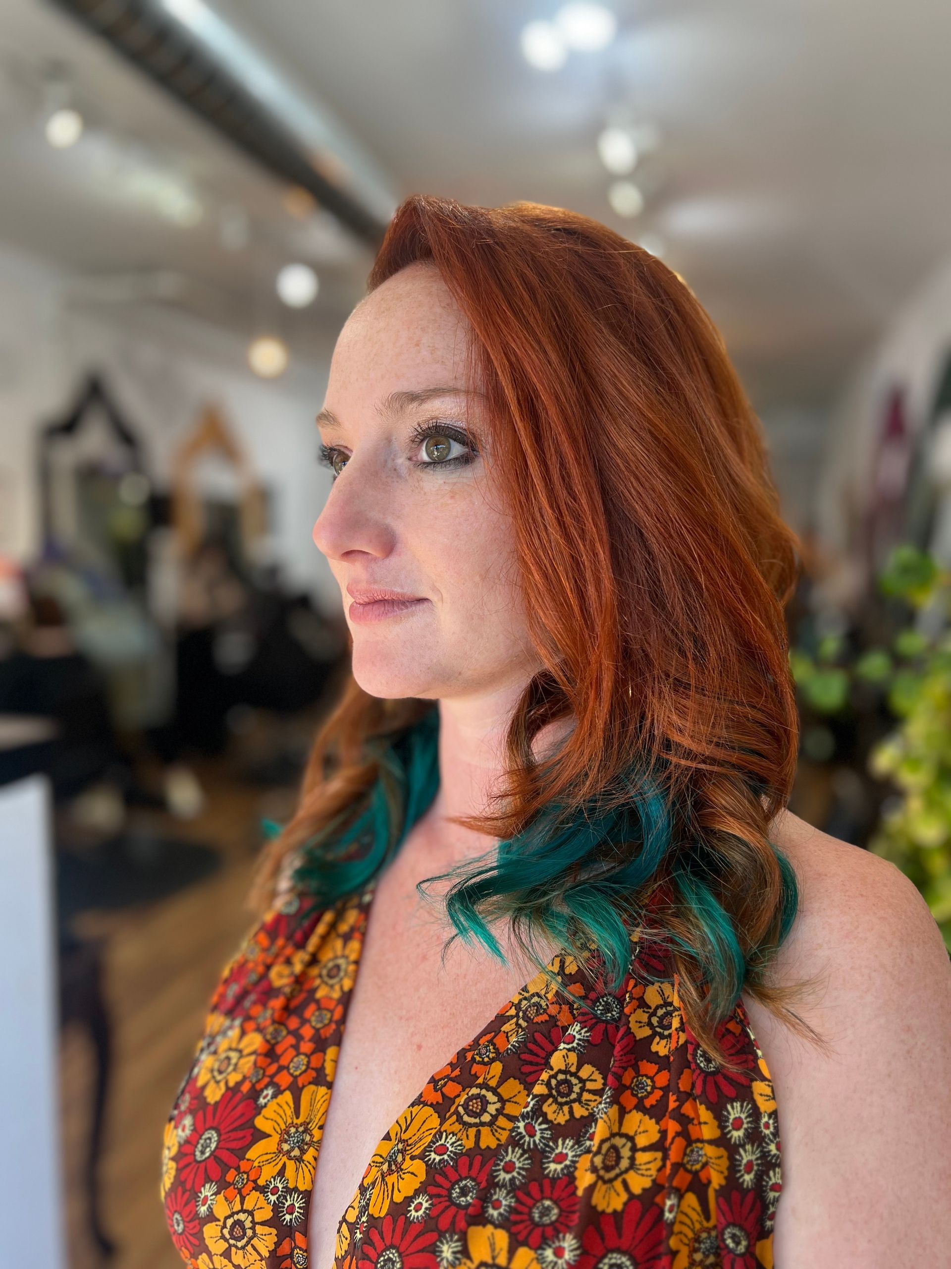 A woman with red hair and green hair is standing in a salon.