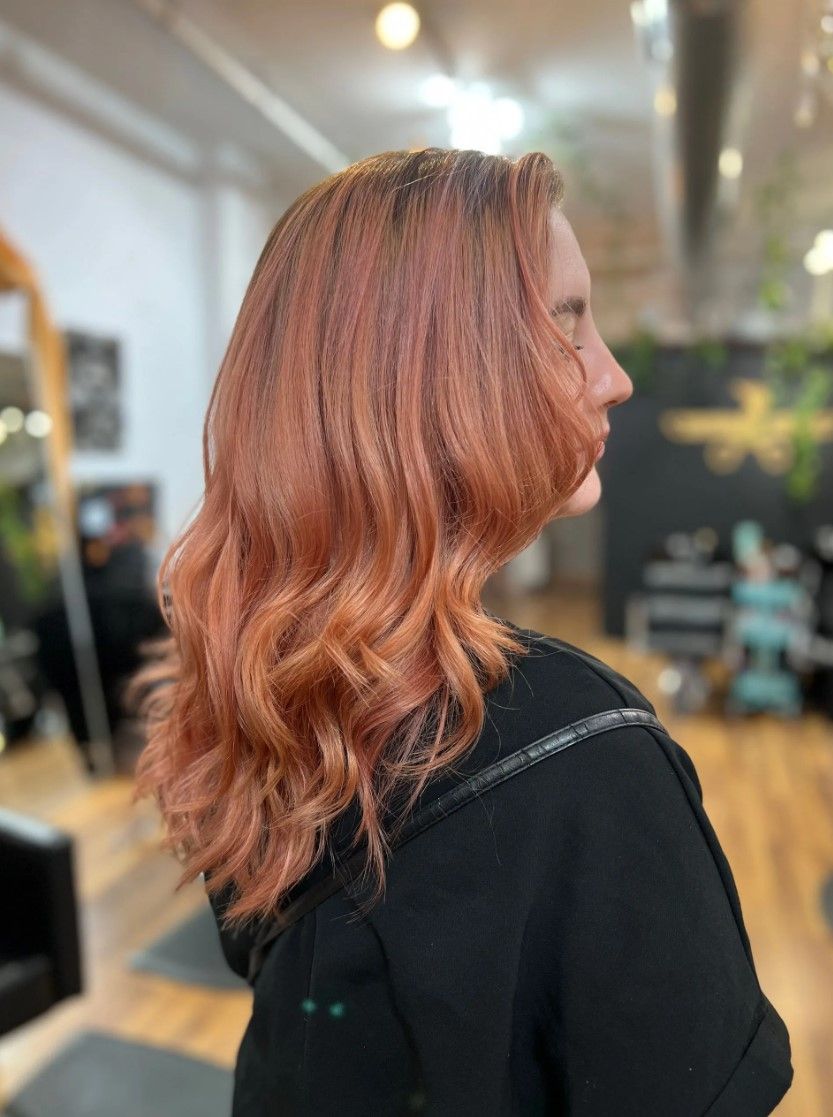 Woman with wavy, reddish-orange hair in a salon setting, wearing a black top.