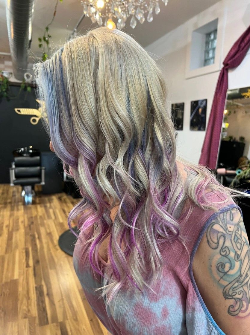 Woman with wavy, multi-toned hair, including blonde, purple, and pink, in a salon.