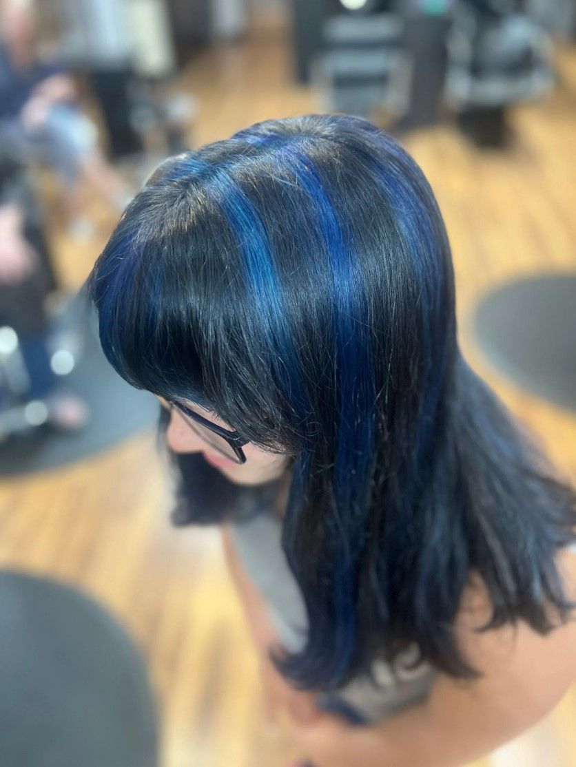 Woman with dark hair, blue highlights, in a hair salon.