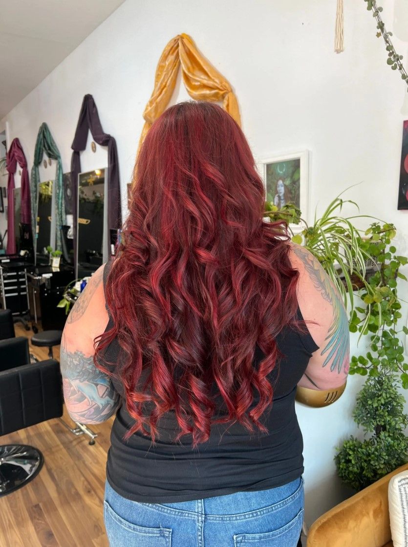 Person with long, wavy red hair in a salon; wearing a black top and jeans.