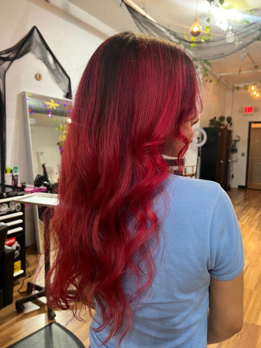 Woman with long red hair, dark roots, stands in a salon.