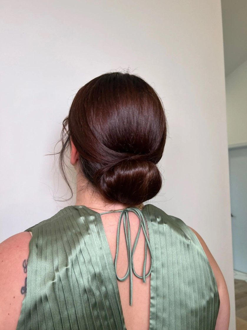 Woman with brown hair in a low bun, wearing a green, satin top with a tie closure.