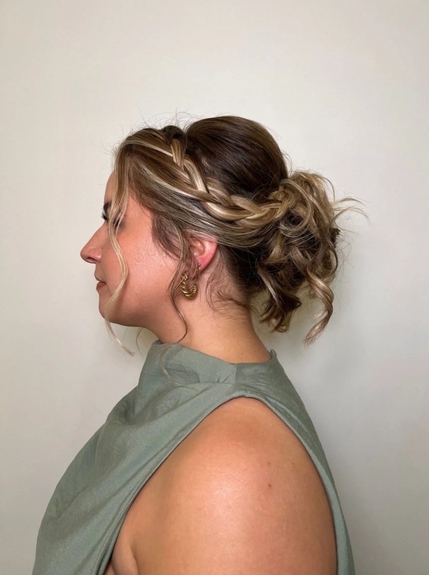 Woman with a side profile, wearing a green top, hair up in an elegant bun with a braided front.