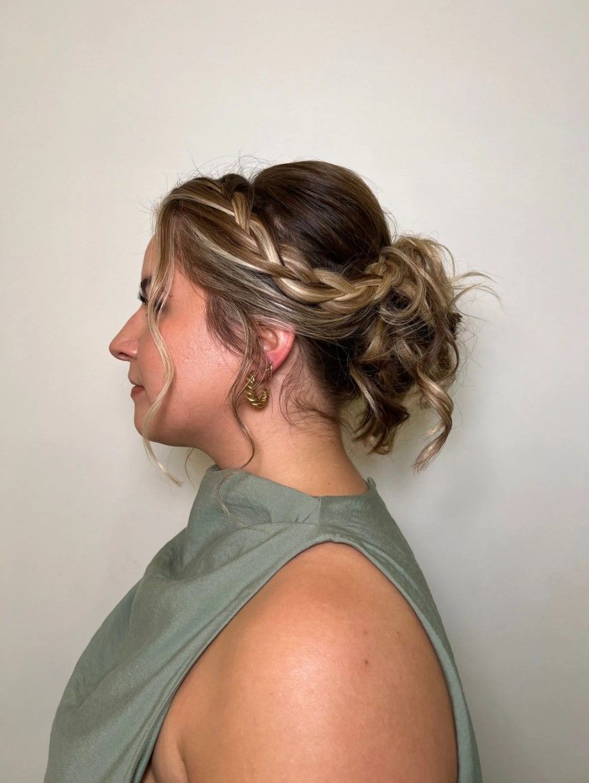 Woman with side profile; updo hairstyle with braided detail, wearing green top.