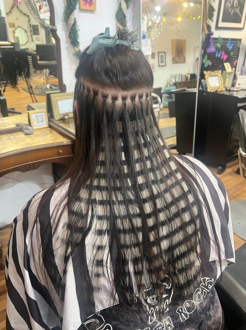 Person with dark hair and hair extensions, sitting in a salon chair. Hair is sectioned in a grid pattern.