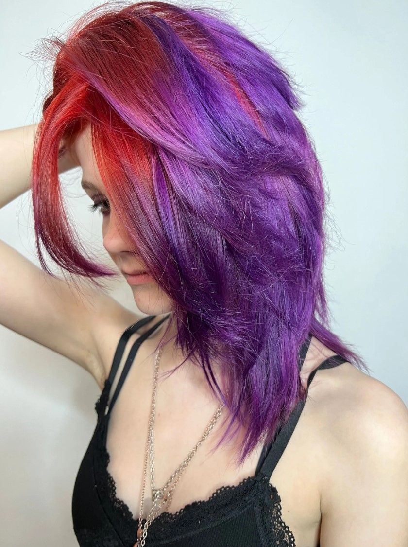 Woman with vibrant red and purple hair, wearing a black top, poses.