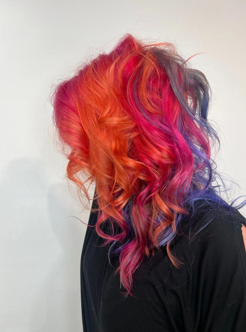 Woman with vibrant, wavy hair in shades of orange, red, pink, and purple.