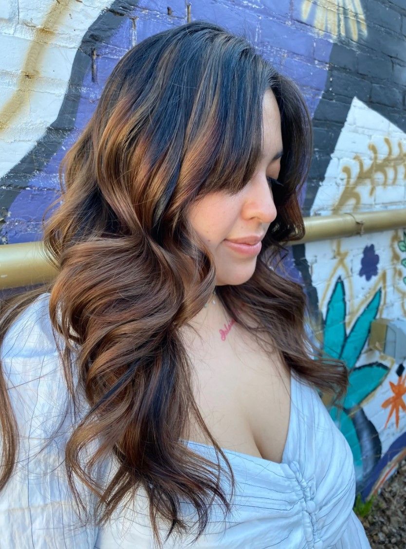 Woman with wavy brown hair, bangs, outdoors, near colorful graffiti.