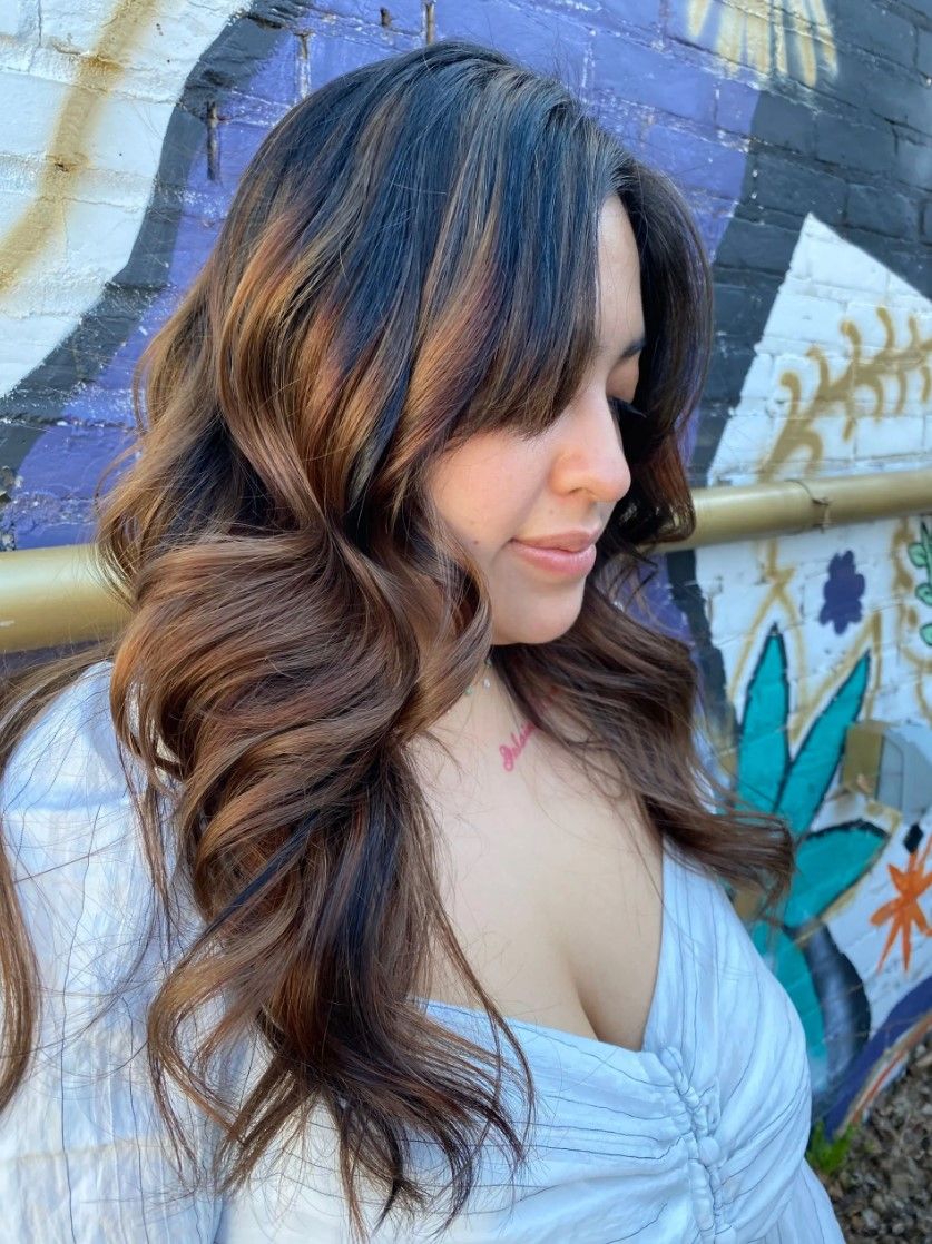 Woman with wavy brown and black hair outdoors, looking down.