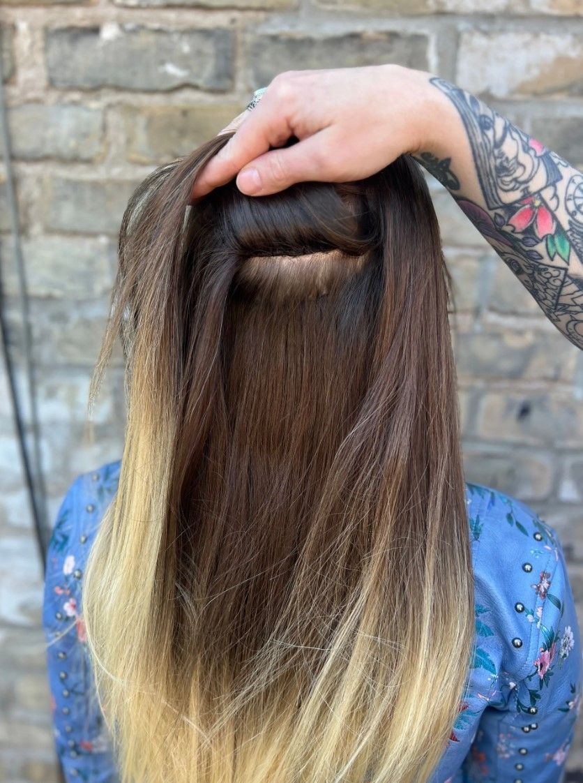 Hand holding up a section of hair. Ombre, brown to blonde, hair. Brick wall background.