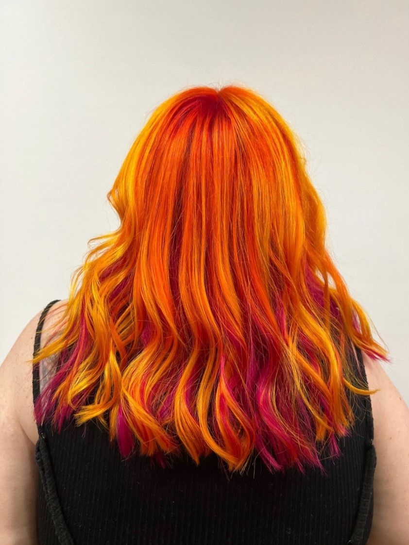 Woman with vibrant orange hair, red roots, and pink highlights; black top.