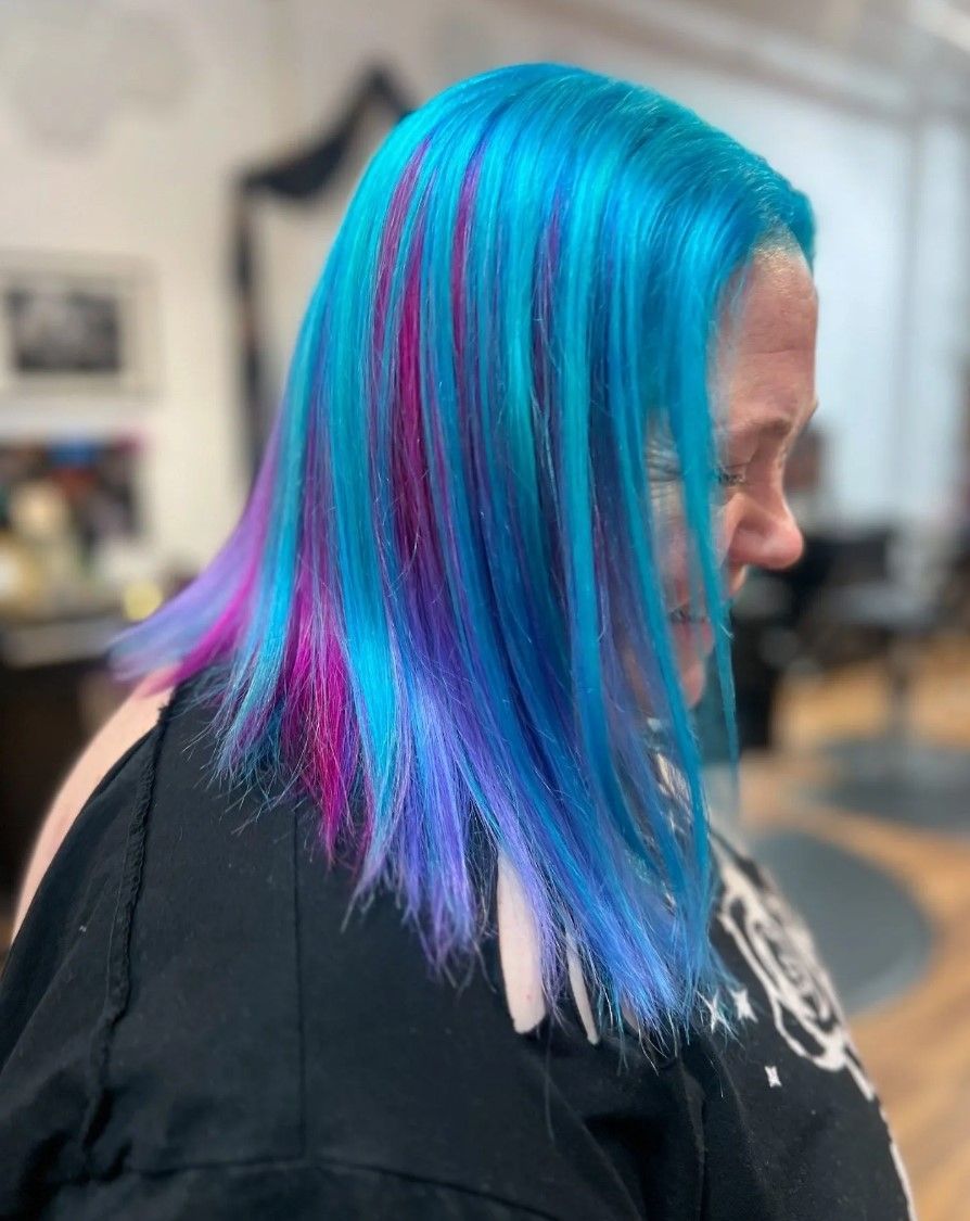 Woman with blue and purple hair with pink streaks in a salon setting.