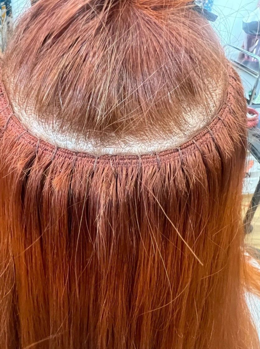 Red hair extensions attached to the scalp with visible micro-beads.