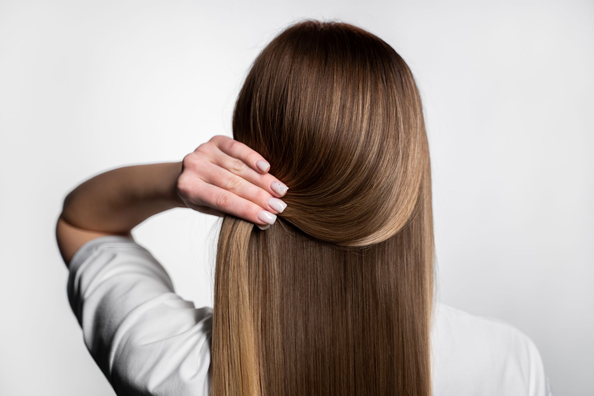 A woman is holding her hair in a ponytail.