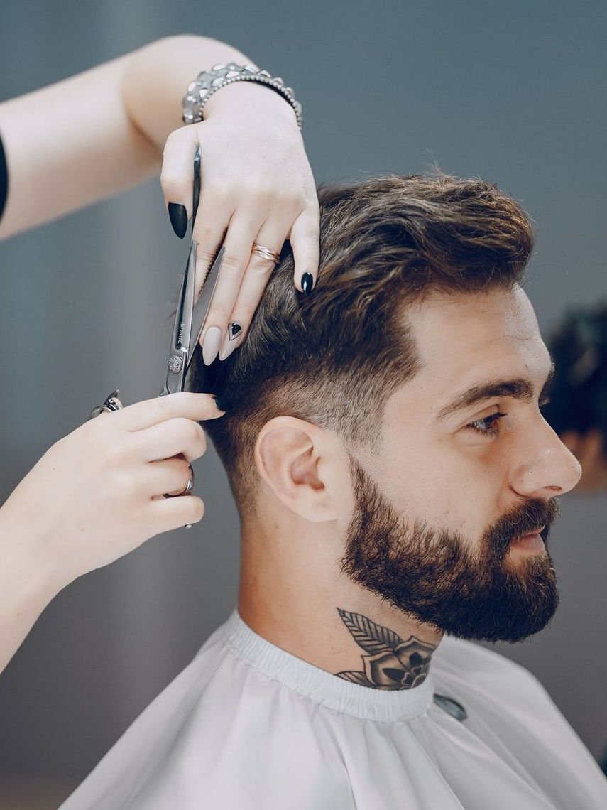 A man with a beard is getting his hair cut by a barber.