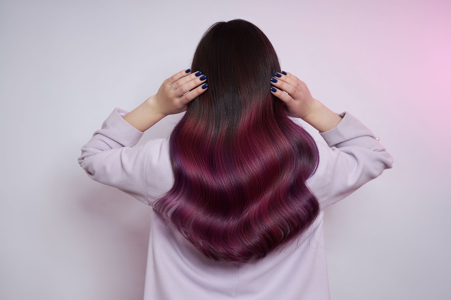 Woman with dark hair styled with purple waves, hands in hair.