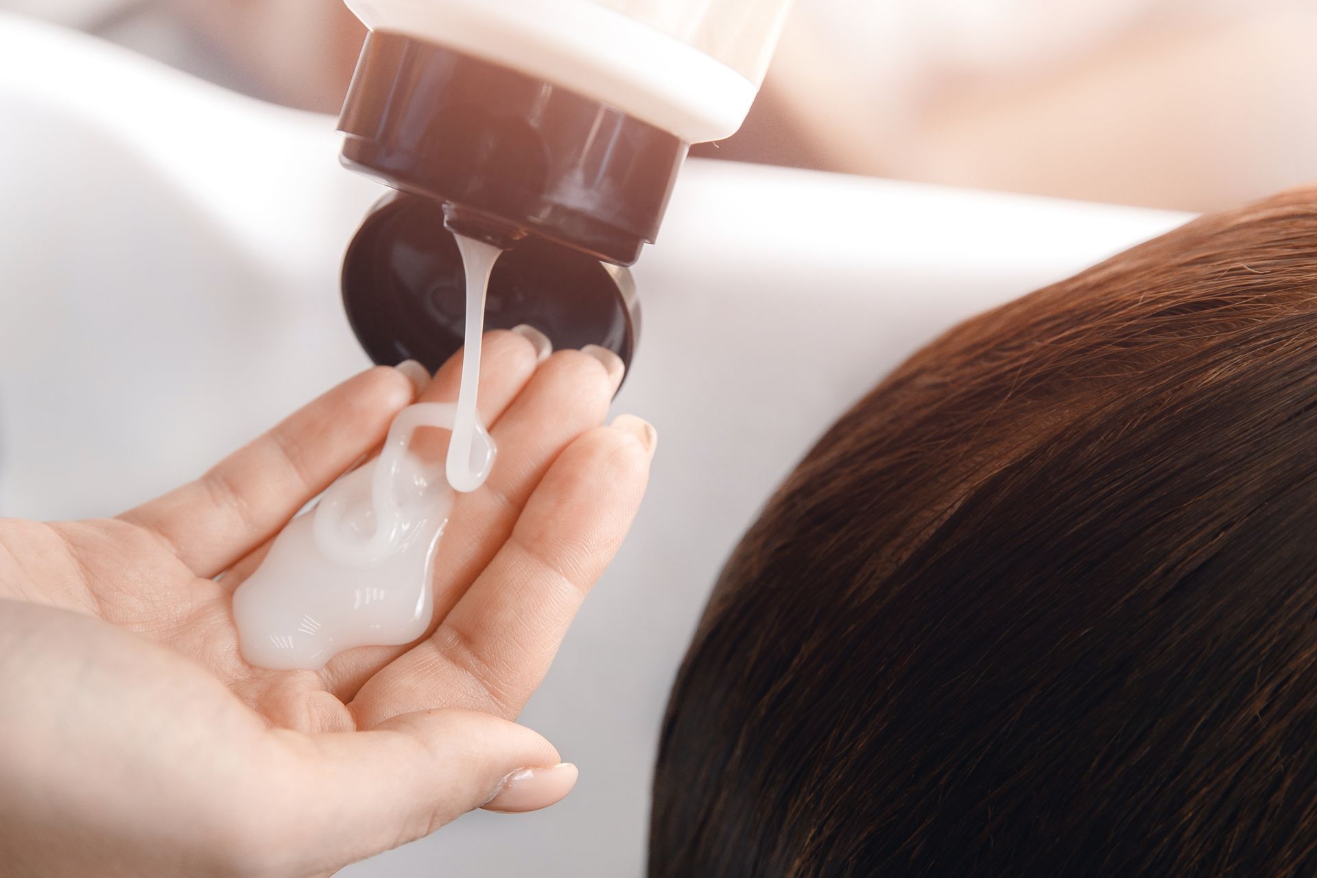 A woman is getting her hair washed at a salon and holding a bottle of shampoo in her hand.