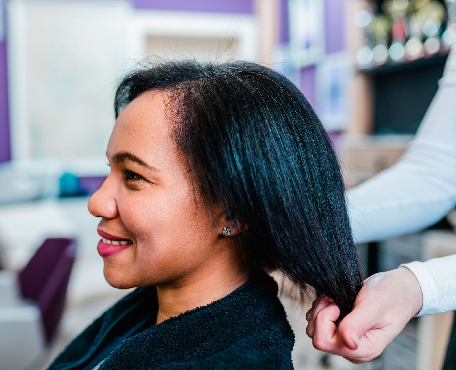 Woman smiling while stylist holds her straight, black hair at salon.