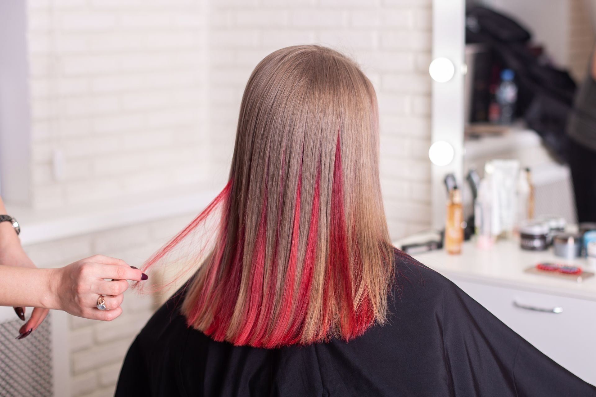 A woman is getting her hair cut by a hairdresser with red highlights.