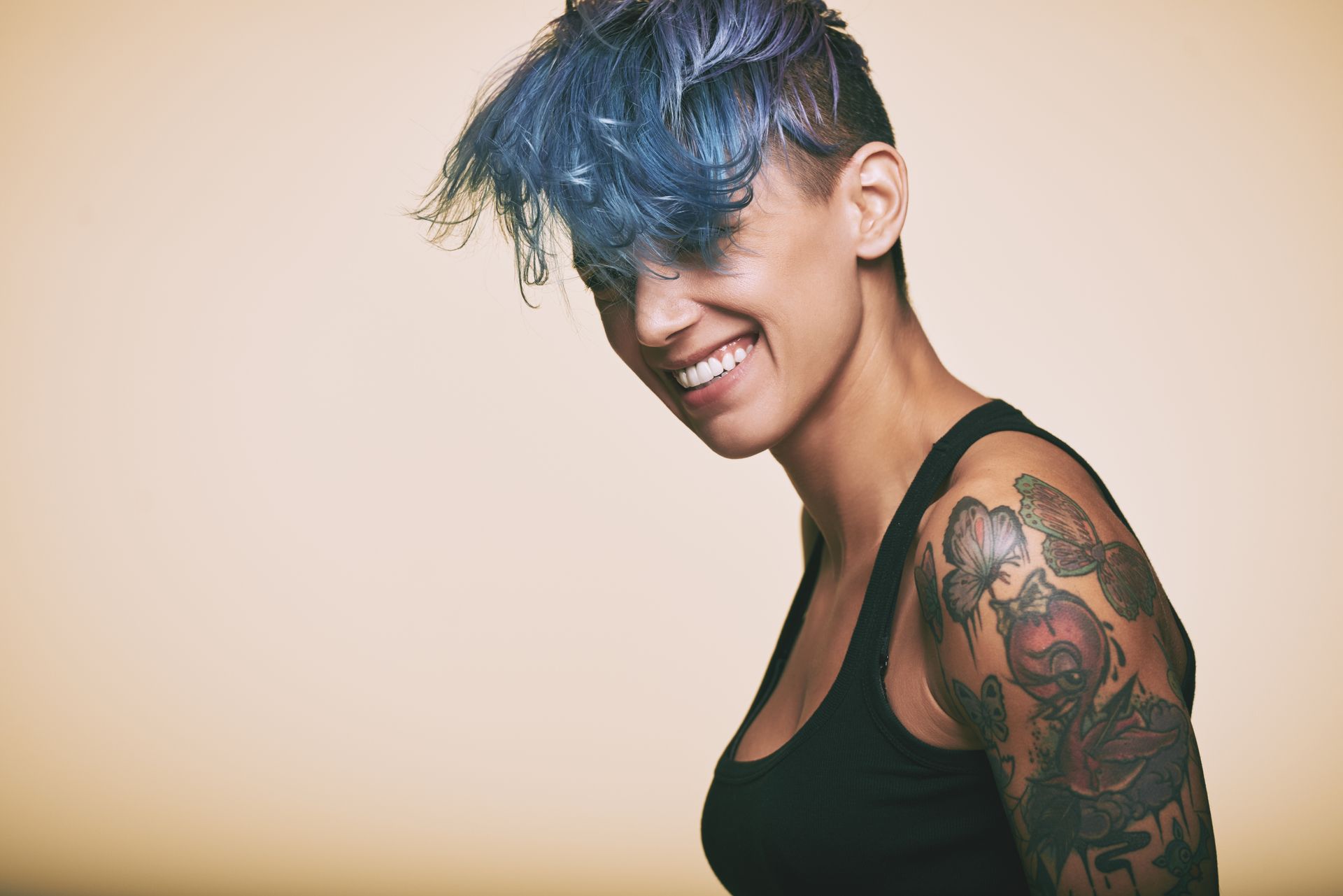 A woman with blue hair and tattoos on her arm is smiling.