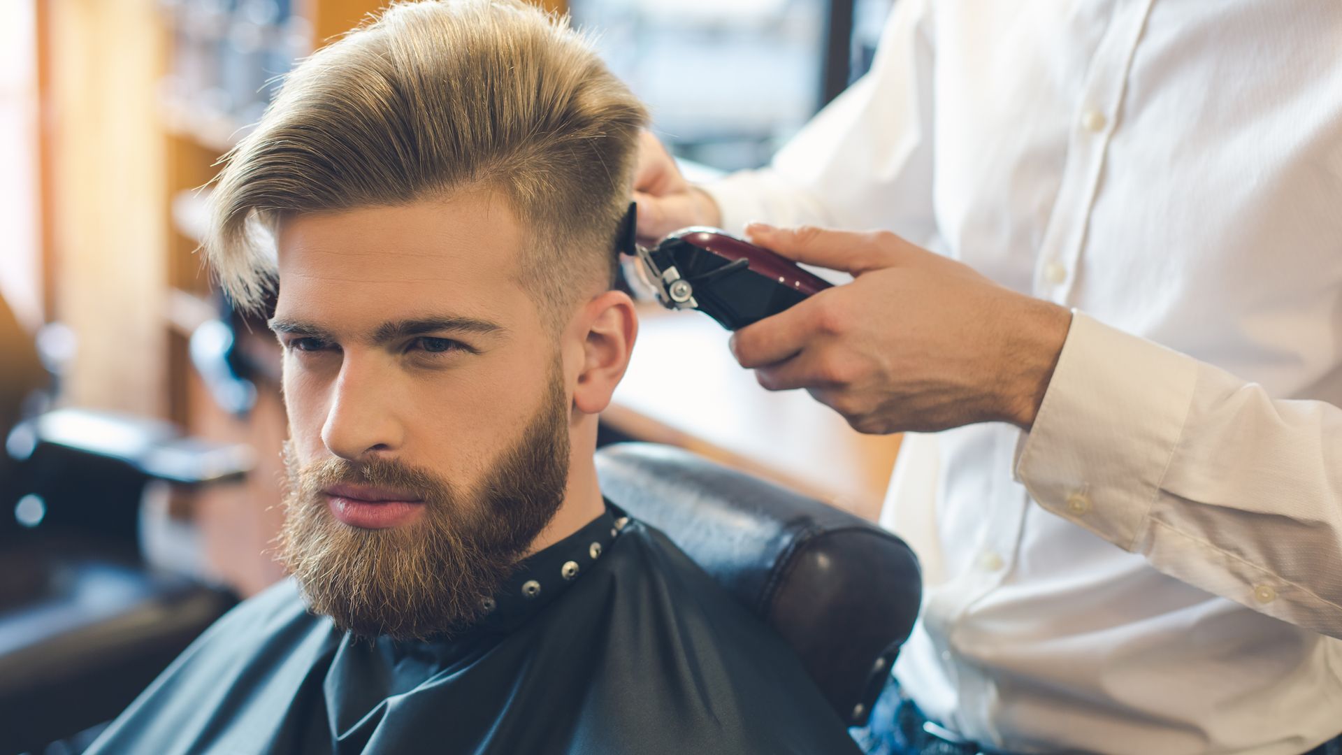 A man with a beard is getting his hair cut by a barber.