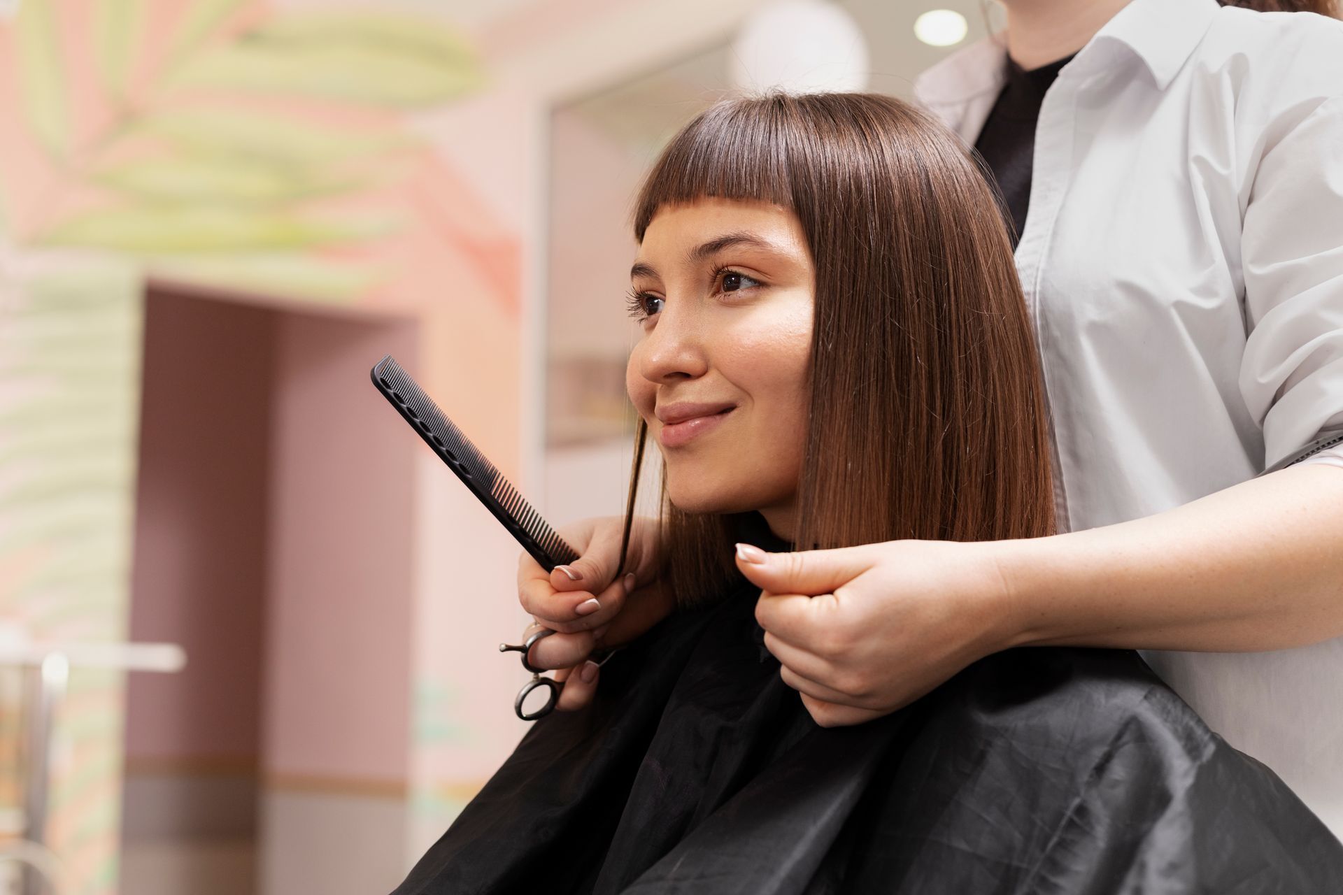 Woman getting her hair cut in a salon, stylist holding scissors, smiling.