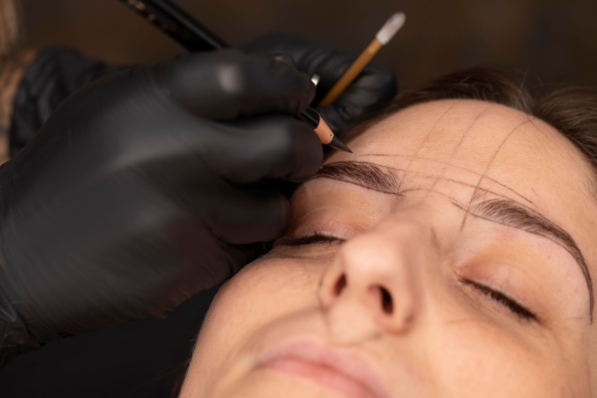 A woman is getting her eyebrows drawn by a tattoo artist.