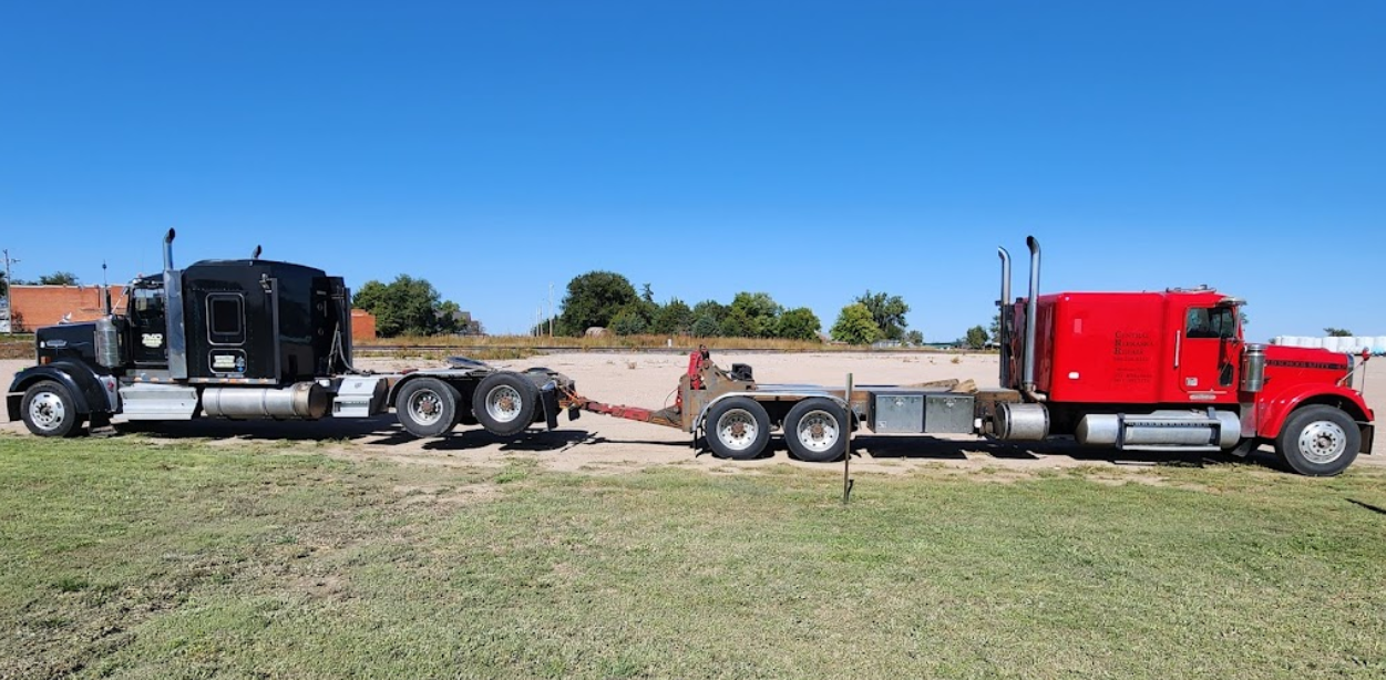 A red semi truck with a trailer attached to it is parked in a grassy field.