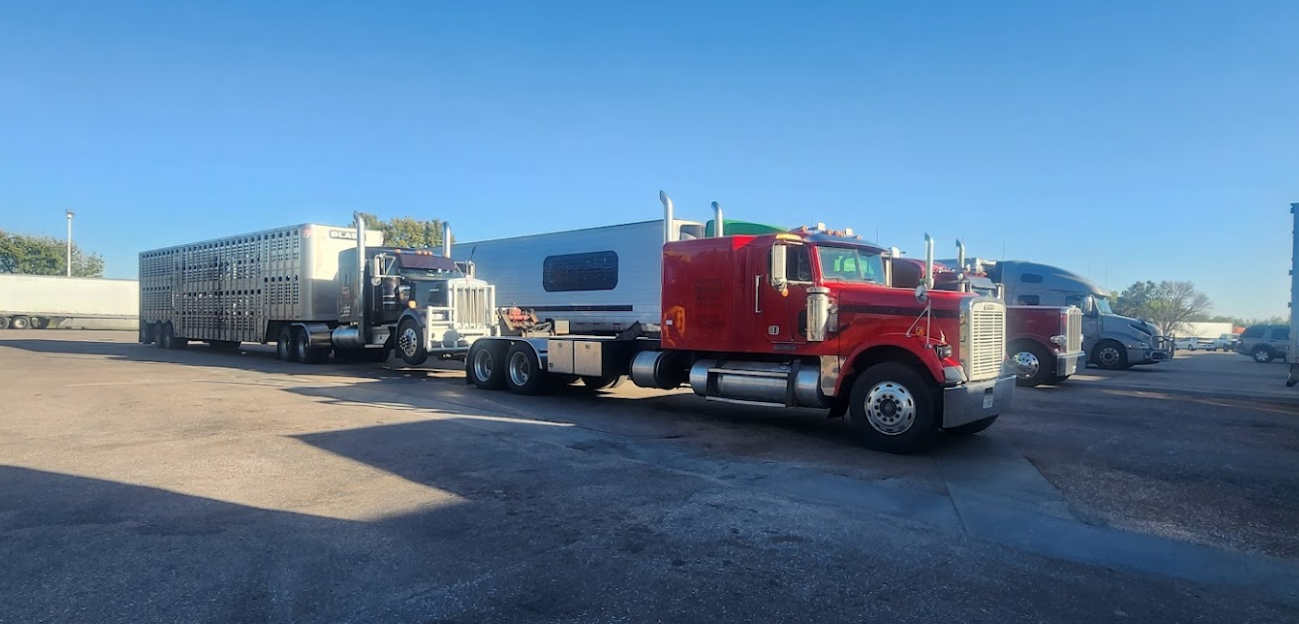 A red semi truck is towing a trailer in a parking lot.