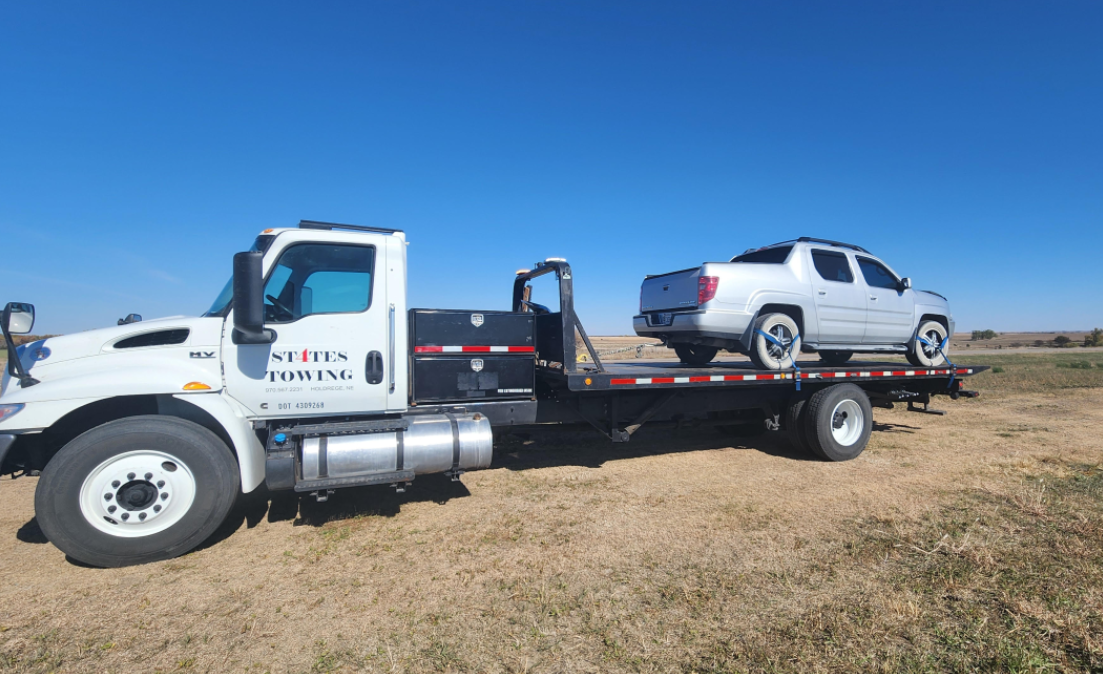 A tow truck is towing a white truck in a field.