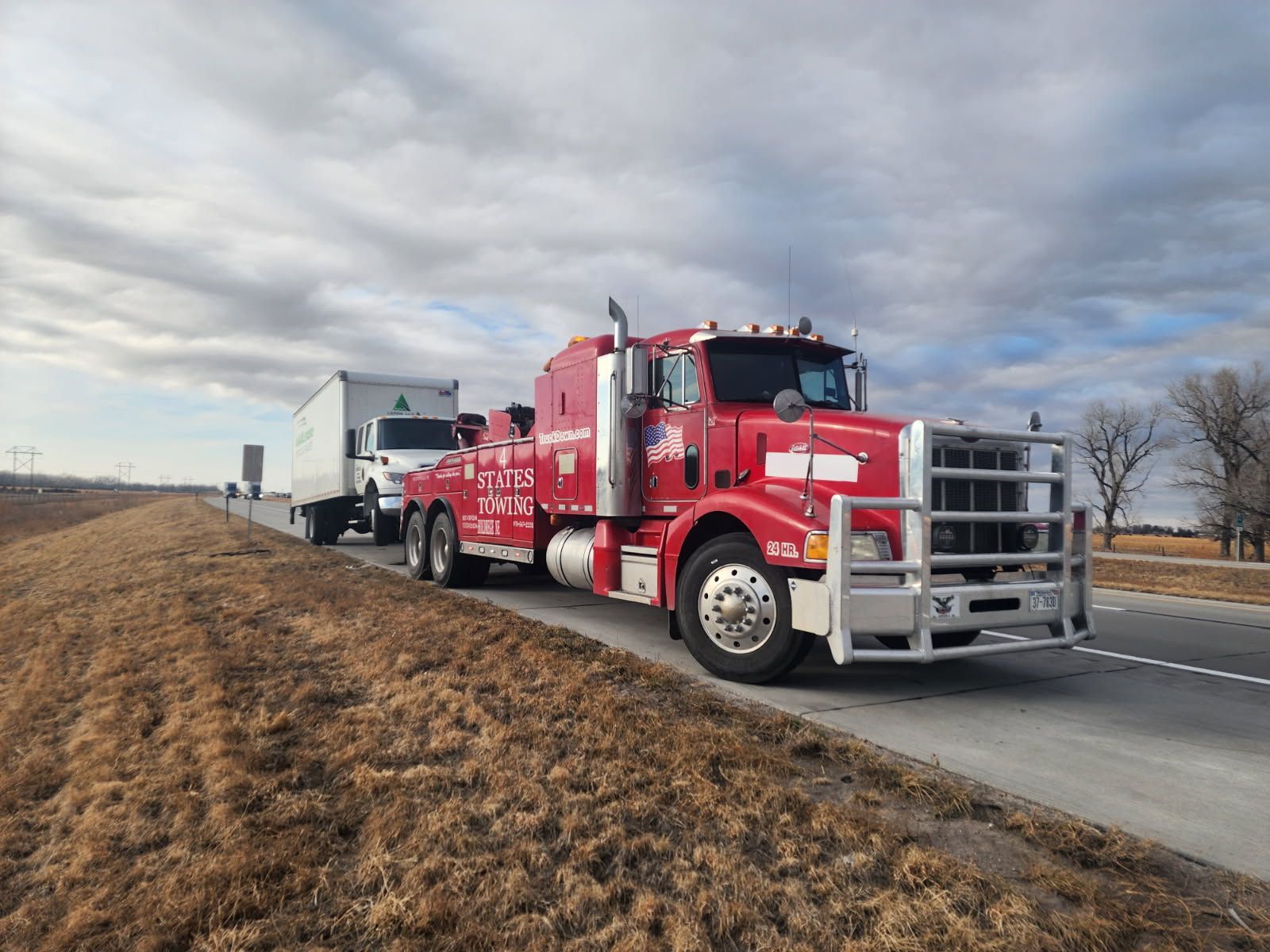A red semi truck with a trailer attached to it is parked in a grassy field.