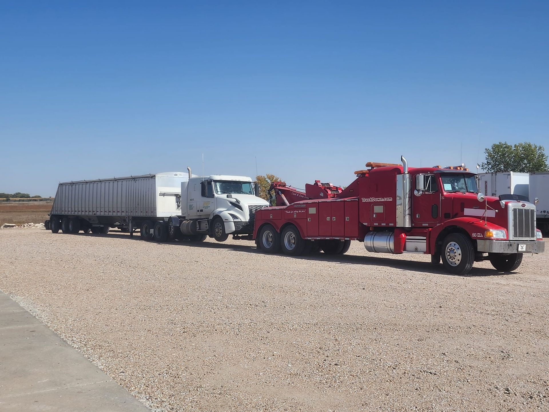 A red tow truck is pulling a white semi trailer
