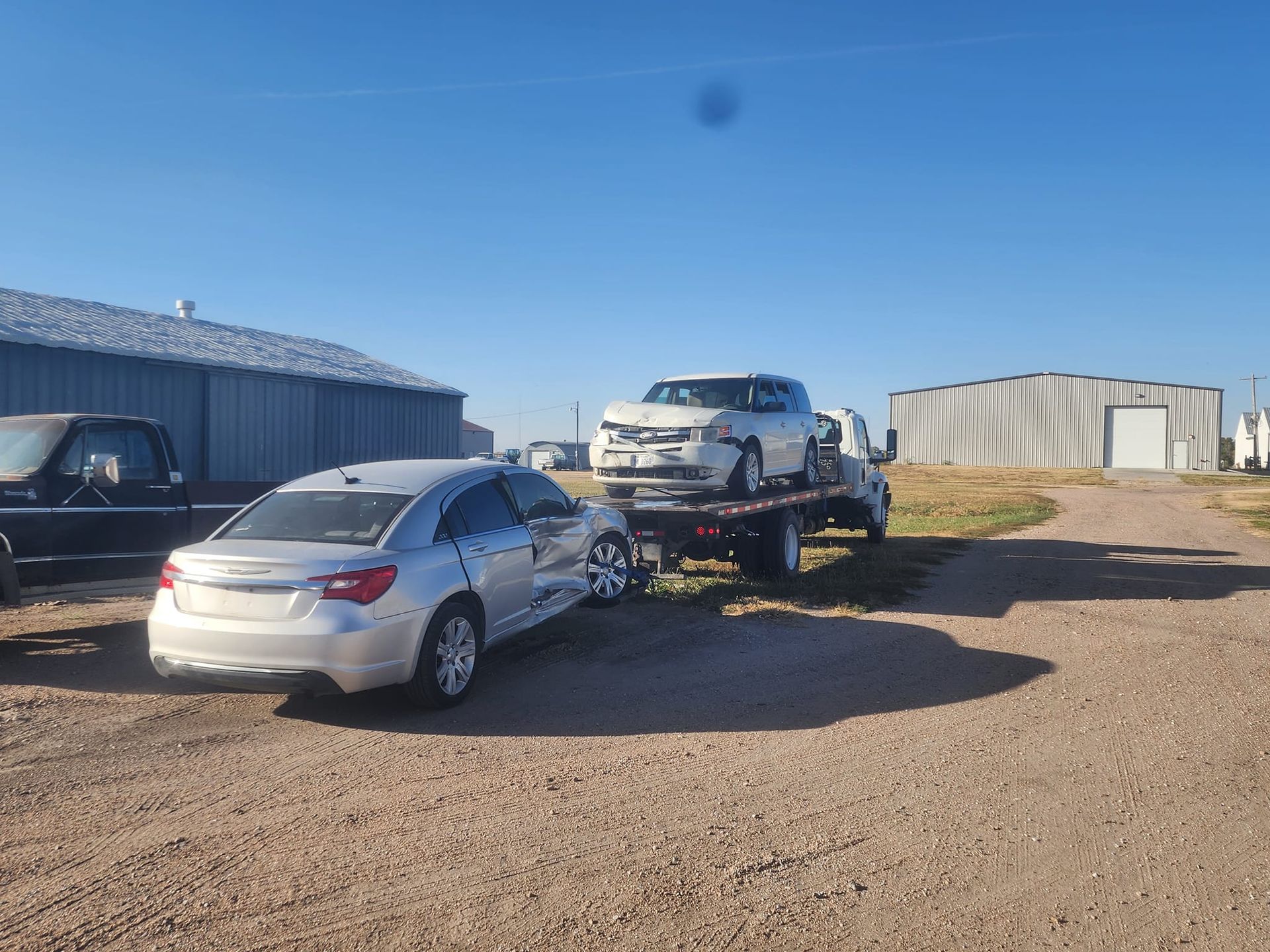 Two cars are being towed by a tow truck on a dirt road.