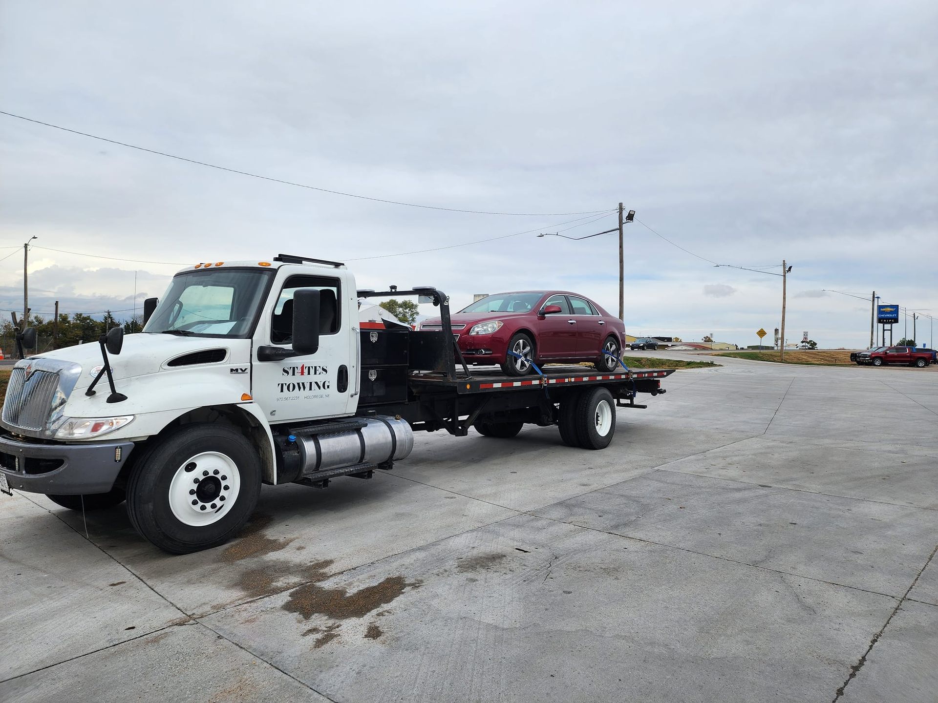 A tow truck is towing a red car in a parking lot.