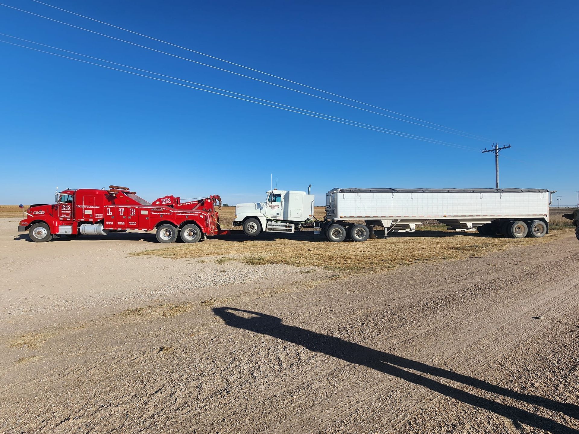Two tow trucks are parked next to each other on a dirt road