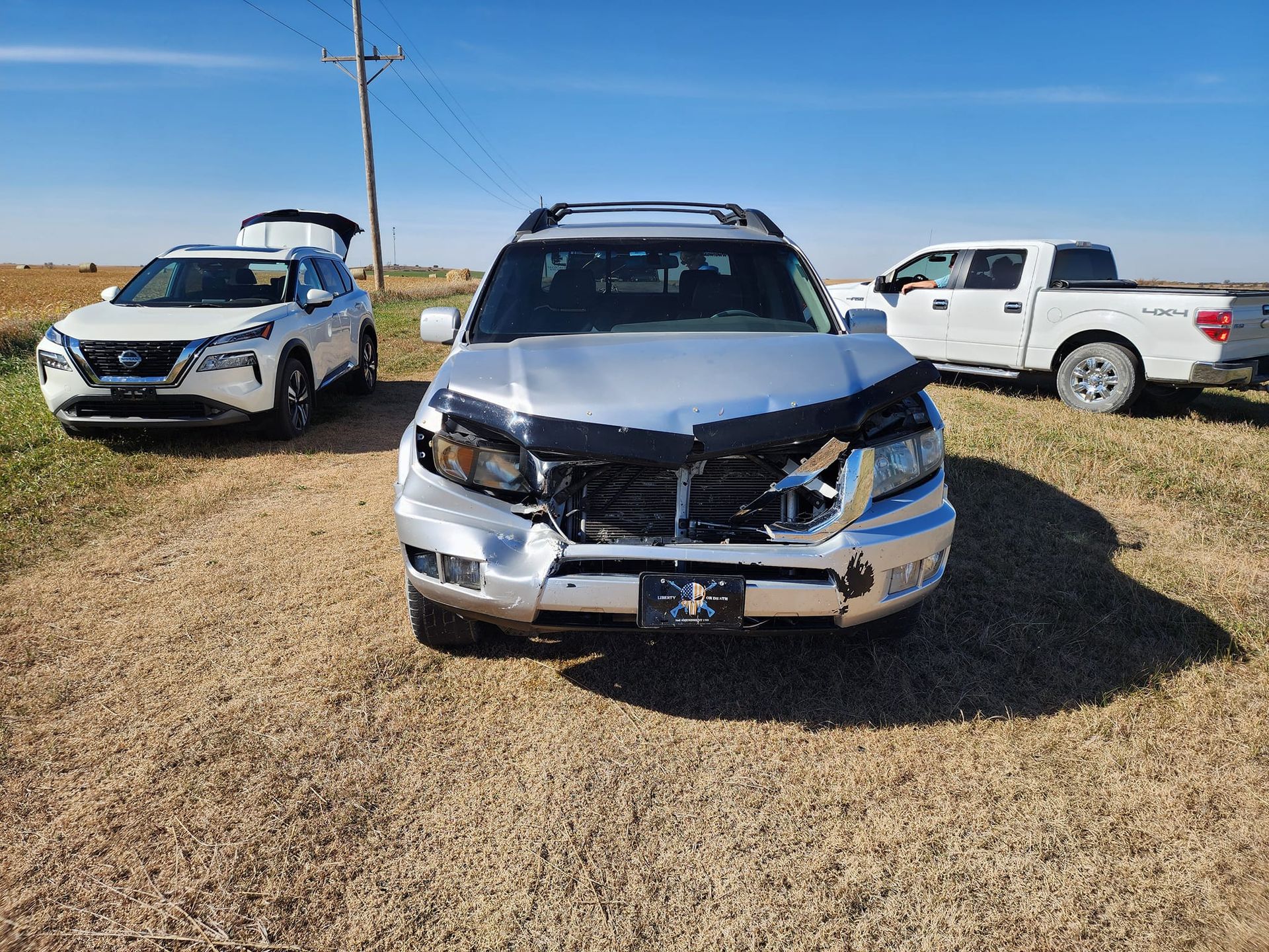 A silver car with a damaged front end is parked next to a white truck.