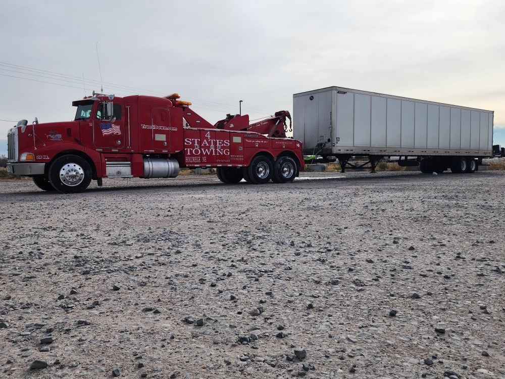 A red tow truck is pulling a white trailer