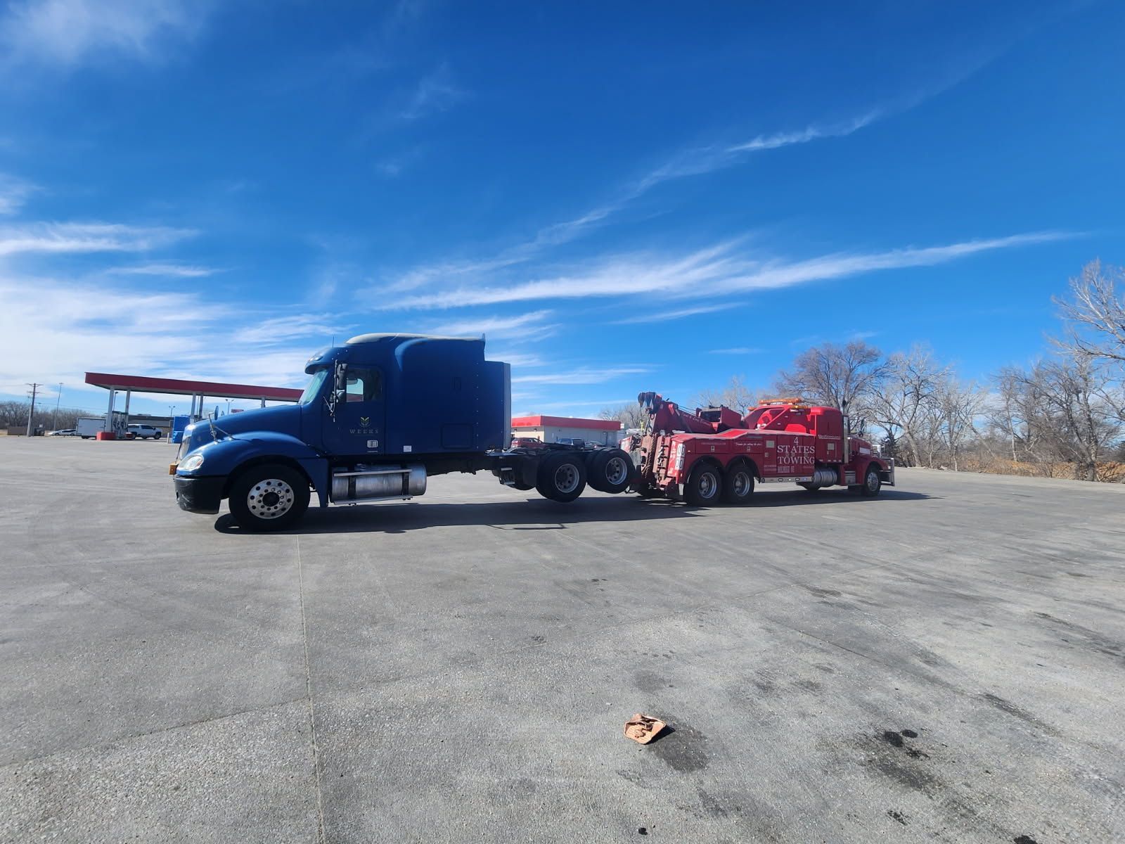 A red semi truck is towing a trailer in a parking lot.