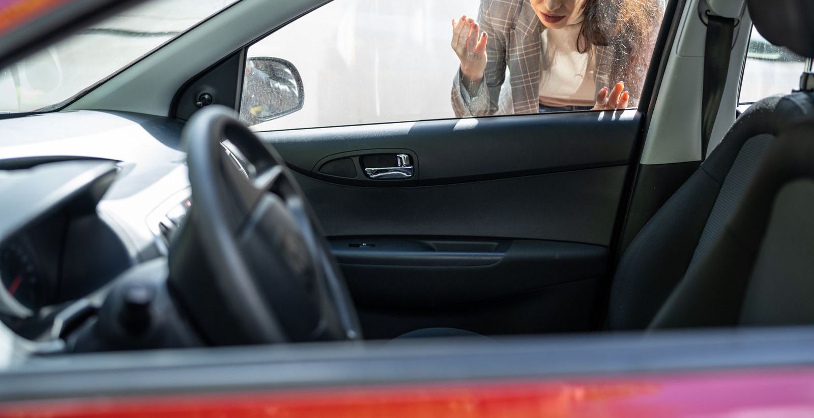 A woman is looking through the window of a car.