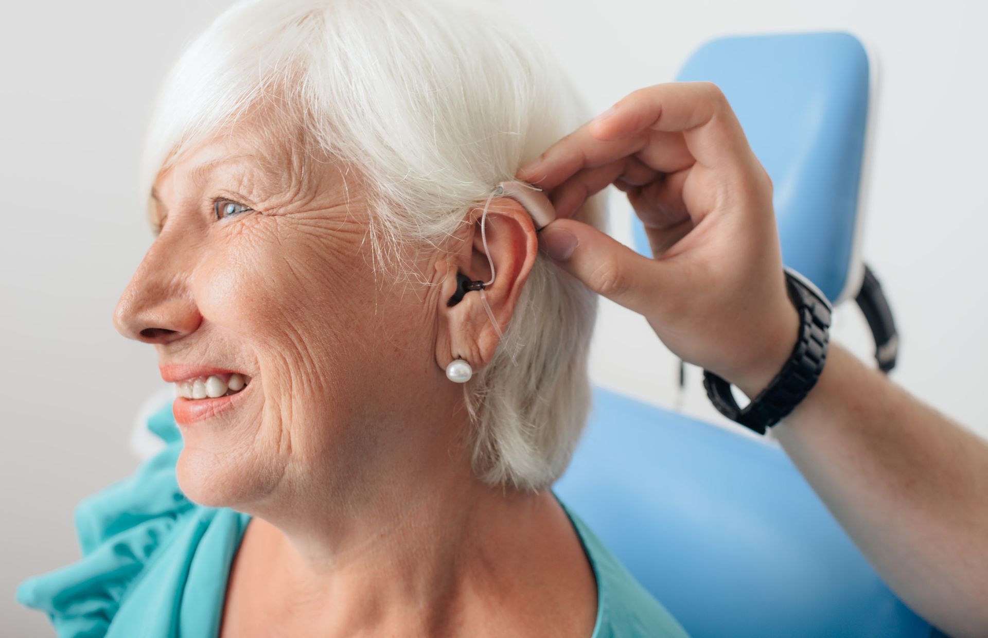 An elderly woman is getting a hearing aid put in her ear.