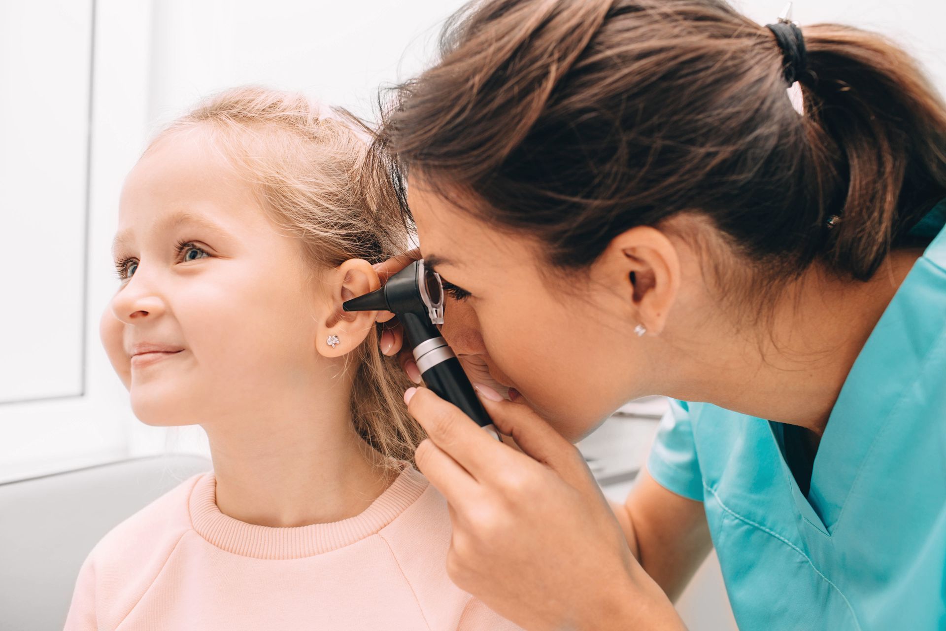 A woman is examining a little girl 's ear with an otoscope.